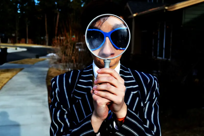 A man wearing glasses holding a magnifying glass in front of him