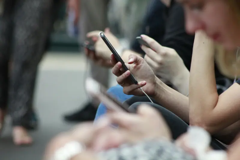 Multiple people sat in a line using modern smart phones